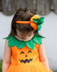 Kislány tök mintás narancssárga jelmezben, zöld levél díszítéssel és tökös hajpánttal