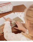 Kislány kreatív naplóval, virágmintás tolltartó és matricák, fa asztalon gyerekszobában