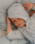 Kisfiú világoskék kapucnis, hímzett gyerek köntösben ágyon fekszik