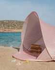 Rózsaszín strand sátor tengerparton, benn piknikkosarak, homokozó játékok a homokban