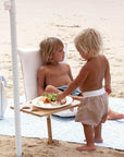 Két kisgyermek piknikasztalnál, strandolnak, homokos tengerparton gyümölccsel.