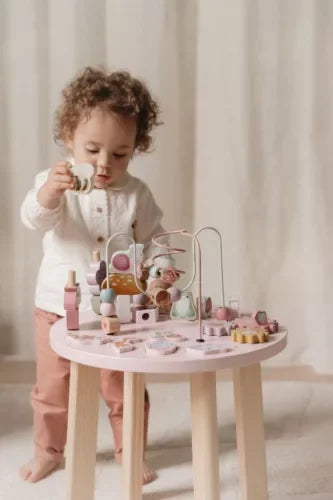 Kisgyermek játszik fa játékokkal és interaktív játékasztallal gyerekszobában.