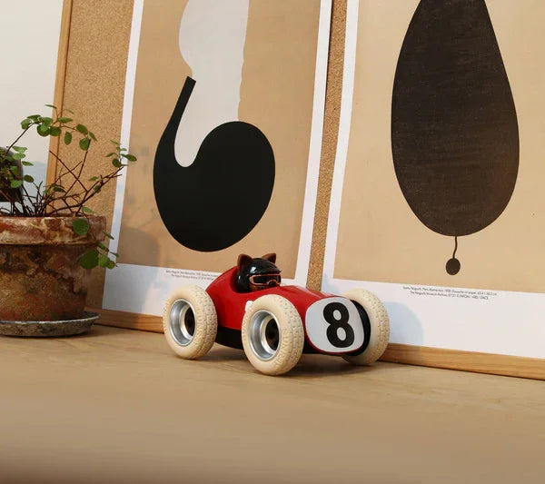 Piros retro stílusú játékautó fehér gumikkal, fa asztalon, dekoratív poszterek előtt