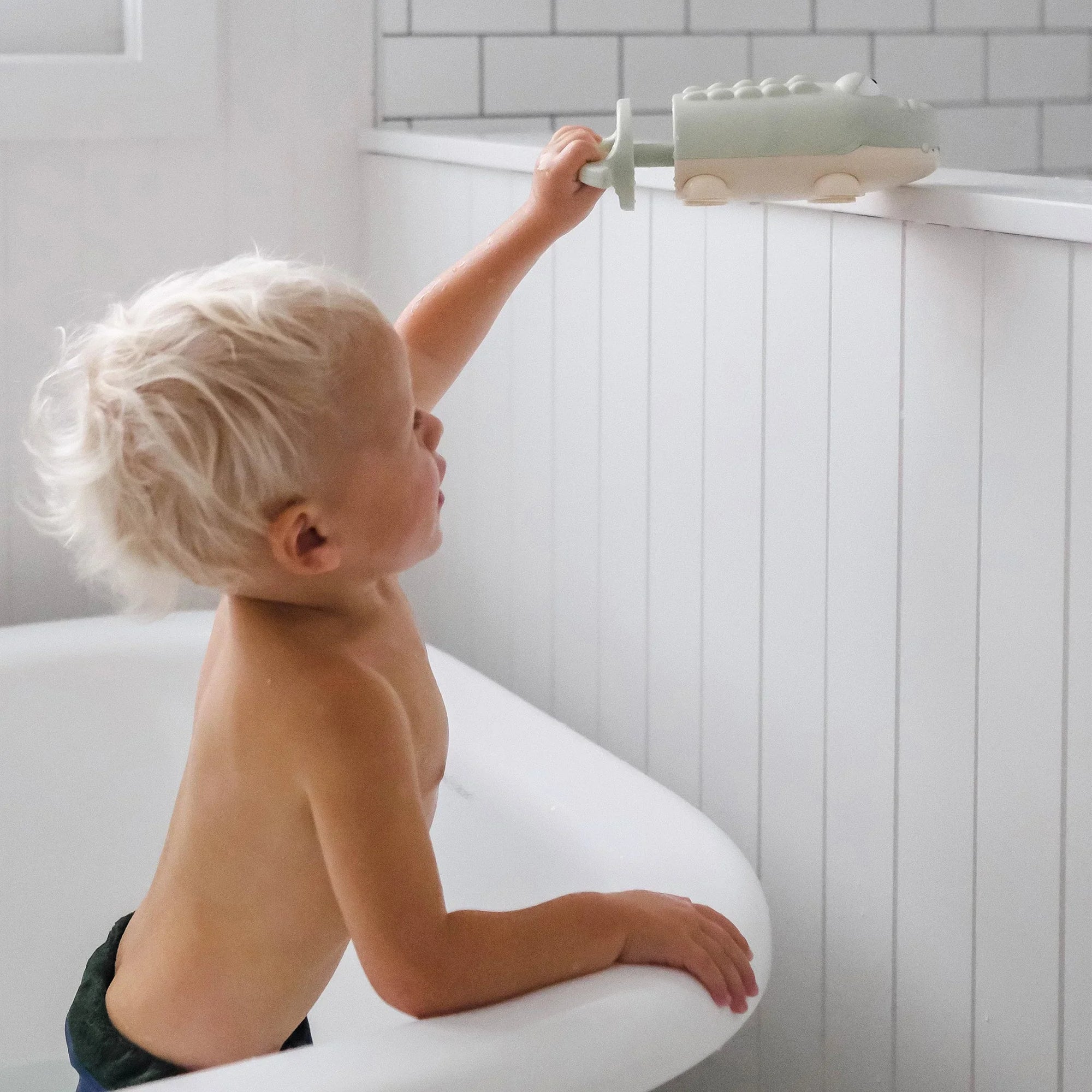 Kisgyermek kádban zöld fürdőjátékkal, világos fürdőszobában játszik.