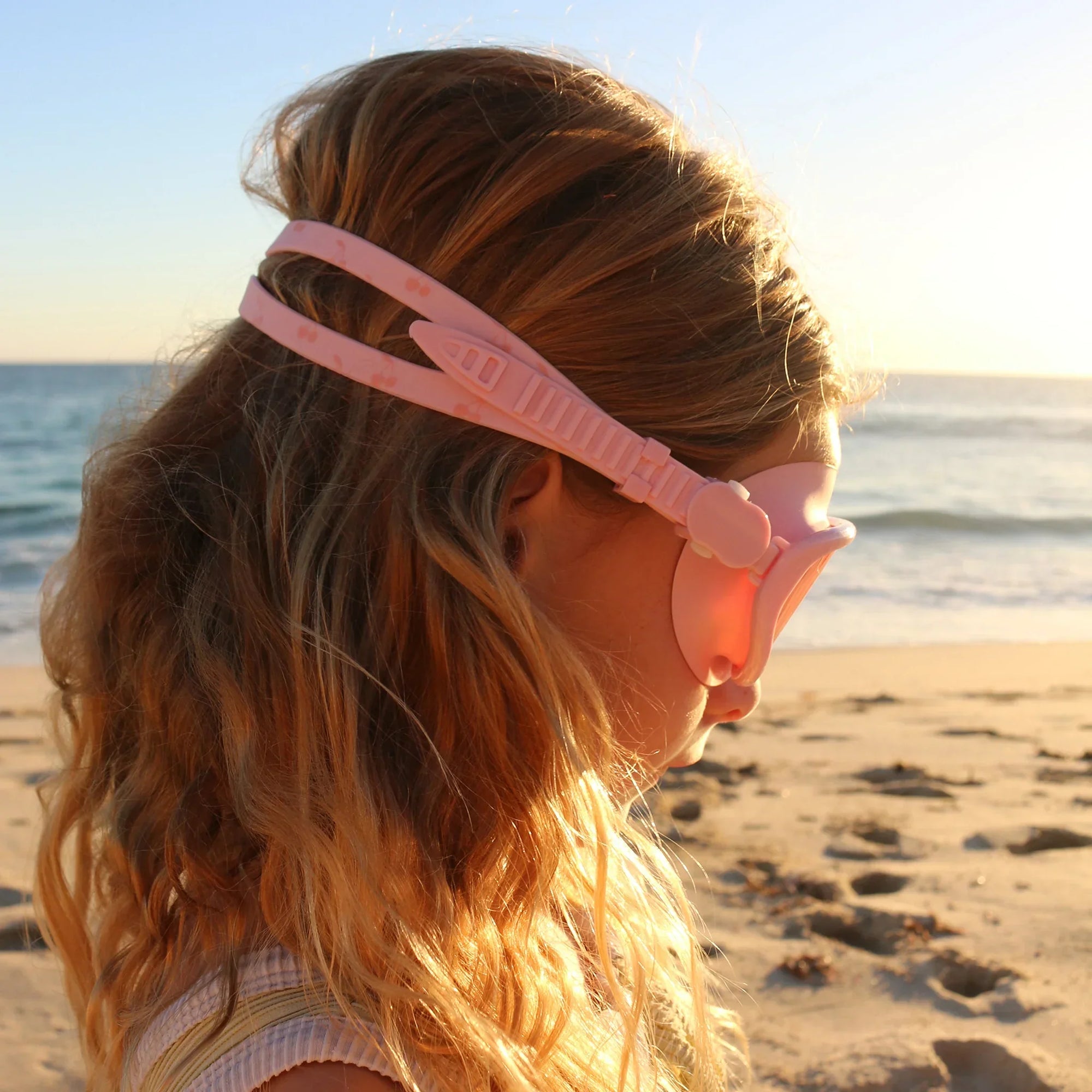 Kislány rózsaszín úszószemüvegben a tengerparton naplementében