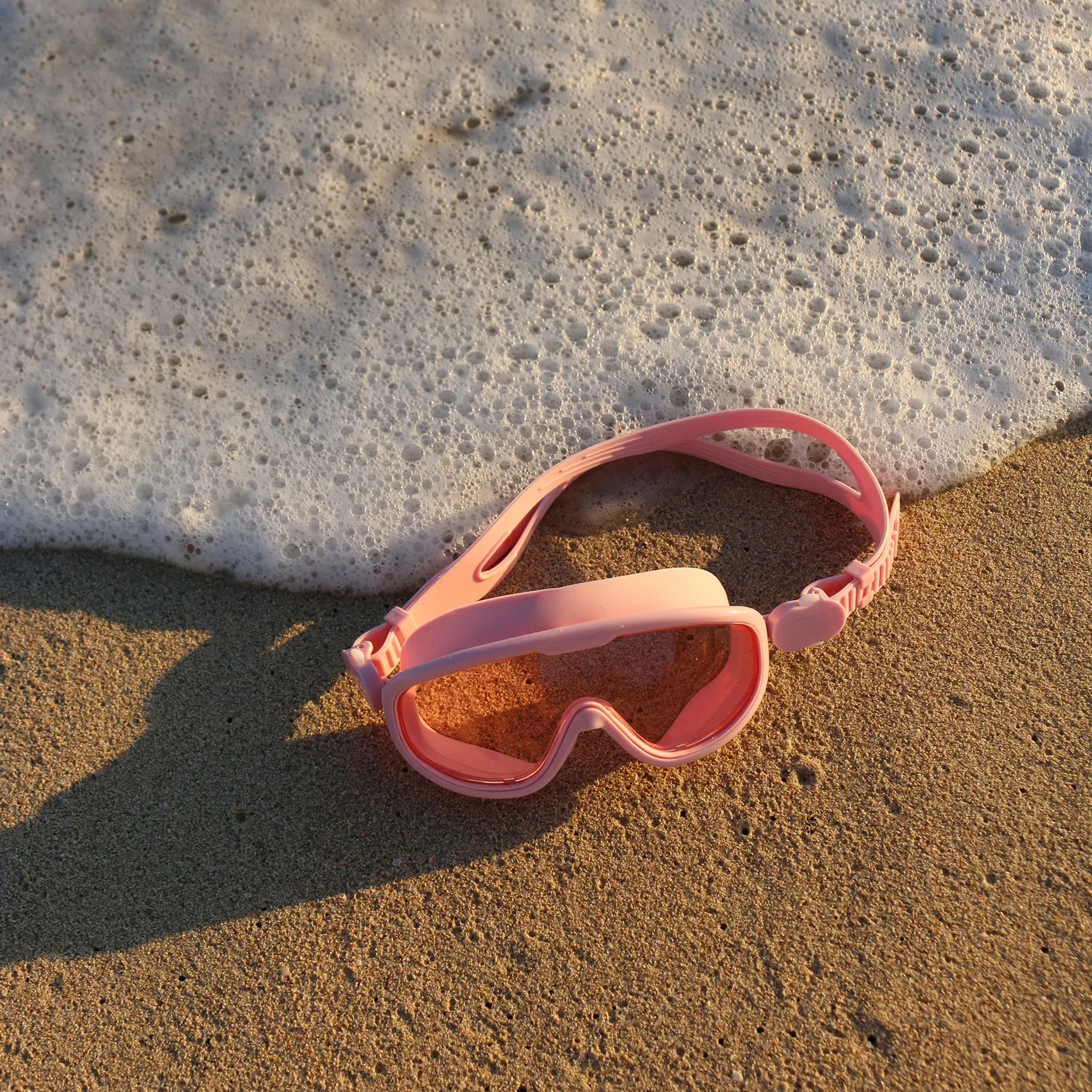 Rózsaszín úszószemüveg homokos tengerparton, habzó víz mellett