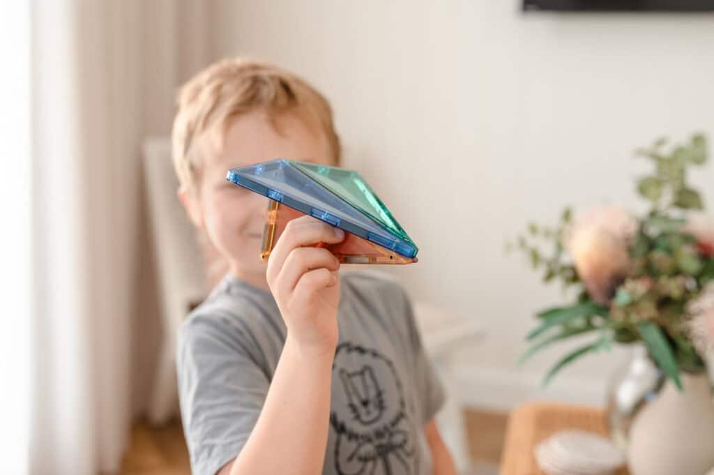 Kisfiú mágneses építőjátékkal játszik világos szobában, kreatív játék közben
